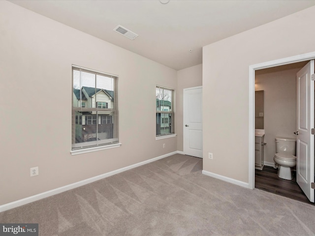 unfurnished bedroom featuring ensuite bathroom, light carpet, and multiple windows