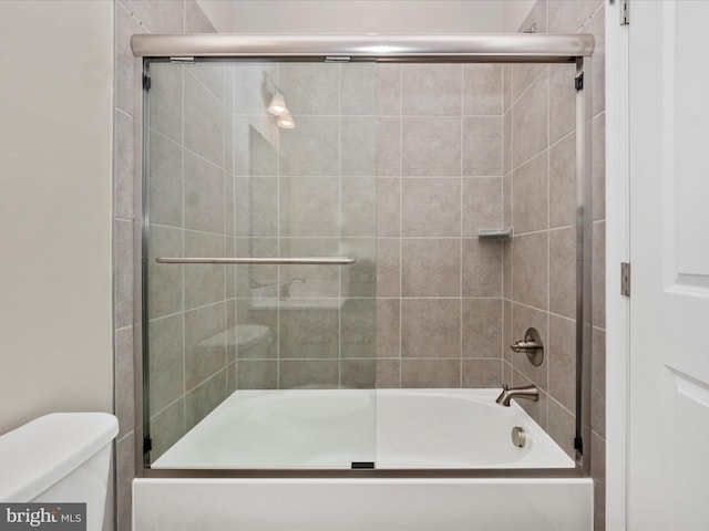 bathroom with toilet and shower / bath combination with glass door