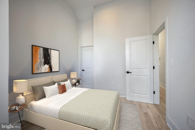 bedroom featuring light hardwood / wood-style floors and a towering ceiling