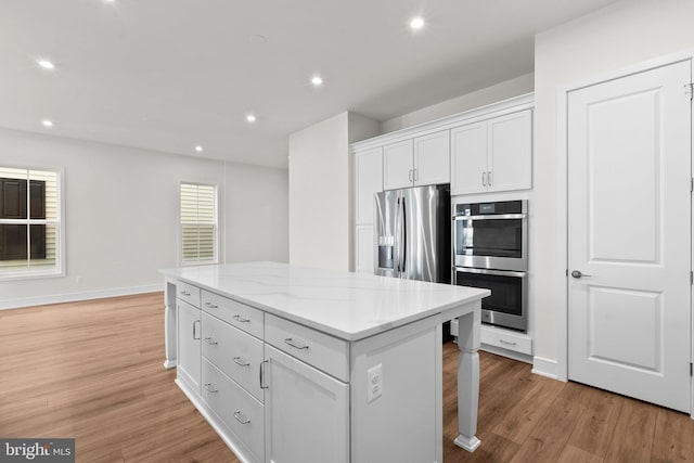 kitchen with a center island, white cabinets, light wood-type flooring, appliances with stainless steel finishes, and light stone counters