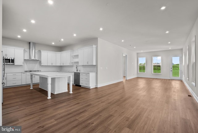 kitchen featuring a center island, wall chimney exhaust hood, appliances with stainless steel finishes, a kitchen bar, and white cabinetry