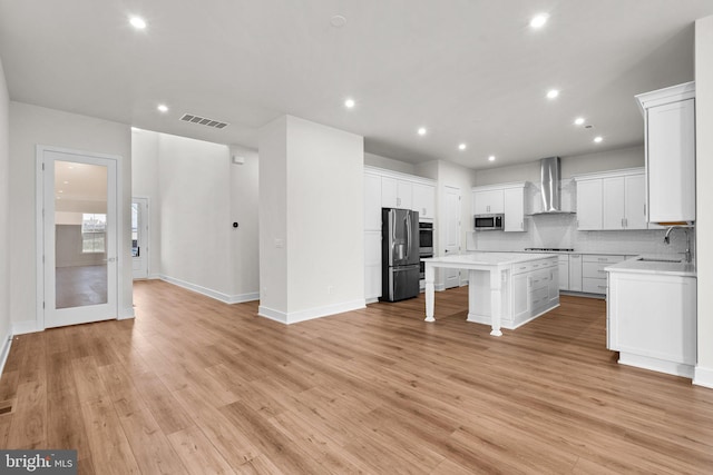 kitchen with wall chimney exhaust hood, a kitchen island, stainless steel appliances, and light hardwood / wood-style floors