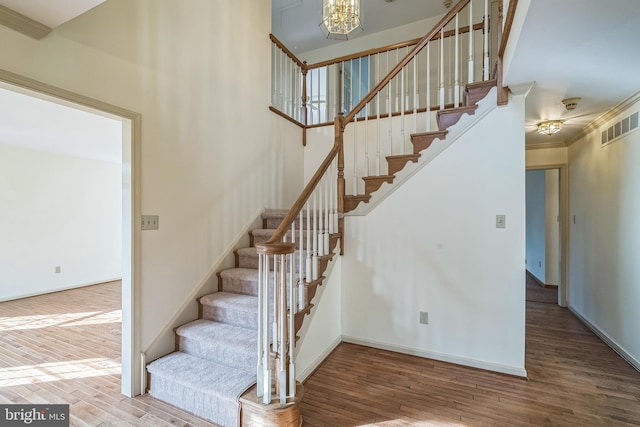 staircase with crown molding, a notable chandelier, and hardwood / wood-style flooring