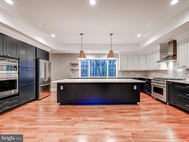 kitchen with wall chimney exhaust hood, premium appliances, light wood-type flooring, and white cabinetry