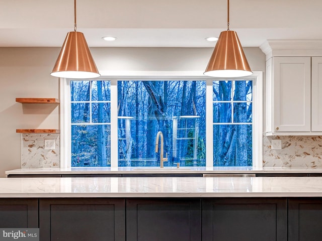 details featuring tasteful backsplash, light stone countertops, sink, and decorative light fixtures