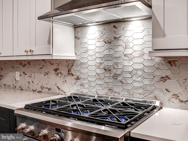 kitchen featuring light stone countertops, tasteful backsplash, wall chimney range hood, high end stainless steel range, and white cabinetry