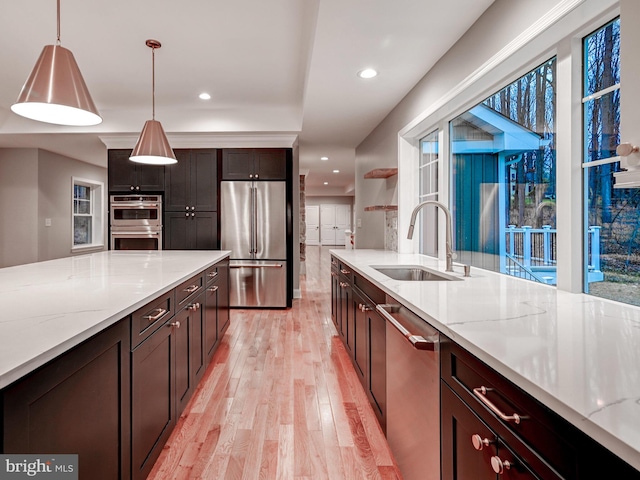 kitchen with light stone counters, stainless steel appliances, sink, pendant lighting, and light hardwood / wood-style floors