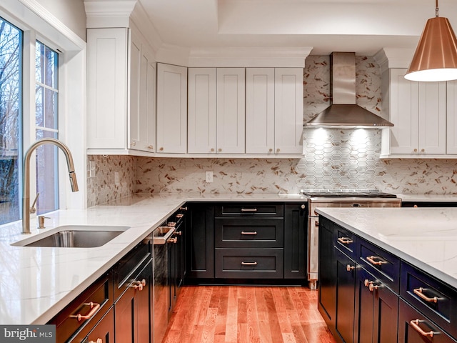 kitchen featuring white cabinets, sink, wall chimney exhaust hood, light wood-type flooring, and light stone countertops