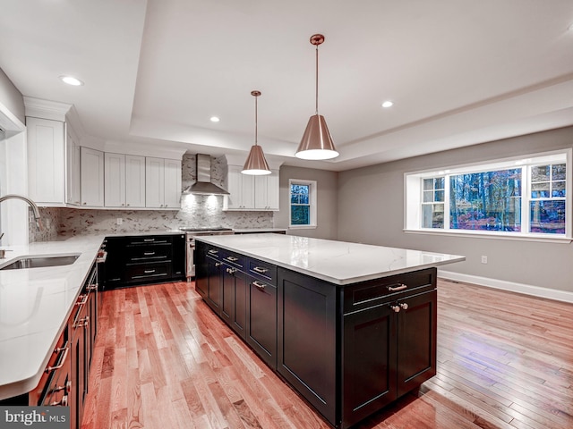 kitchen featuring high end range, sink, wall chimney range hood, light hardwood / wood-style flooring, and a kitchen island