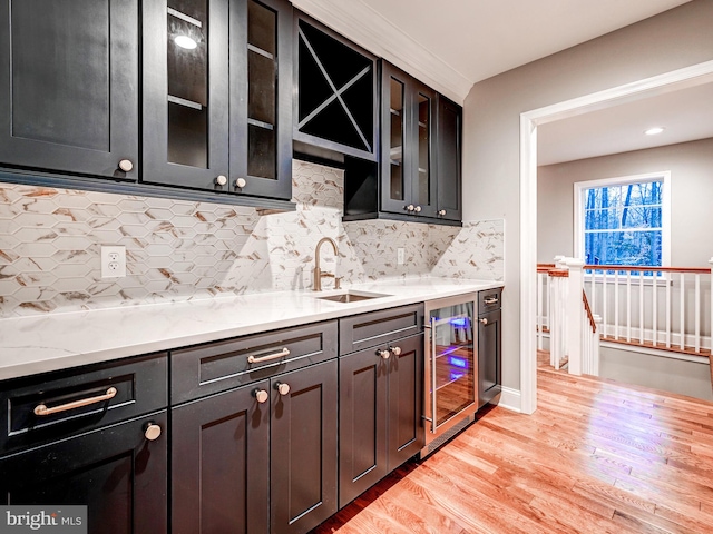 kitchen with light stone countertops, sink, beverage cooler, decorative backsplash, and light wood-type flooring