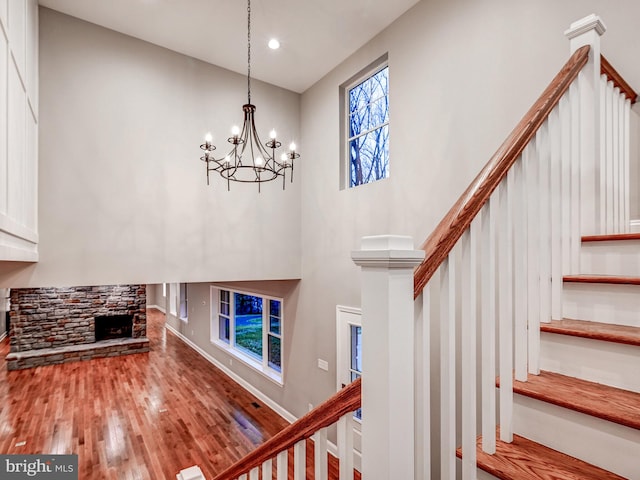 staircase featuring a notable chandelier, wood-type flooring, a fireplace, and a towering ceiling