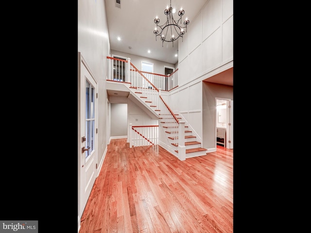 foyer featuring light wood-type flooring, a towering ceiling, and an inviting chandelier