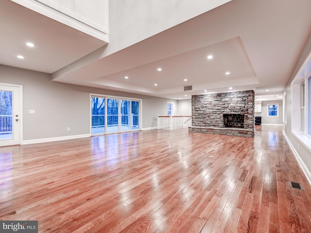 unfurnished living room featuring a tray ceiling, a fireplace, light hardwood / wood-style flooring, and a healthy amount of sunlight