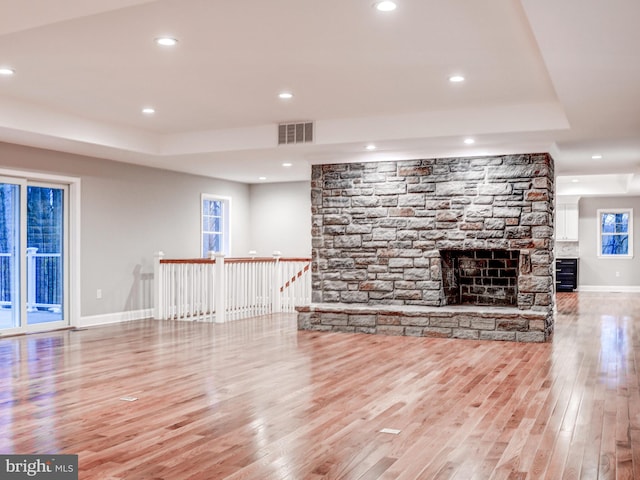 unfurnished living room with a raised ceiling, light hardwood / wood-style floors, and a stone fireplace