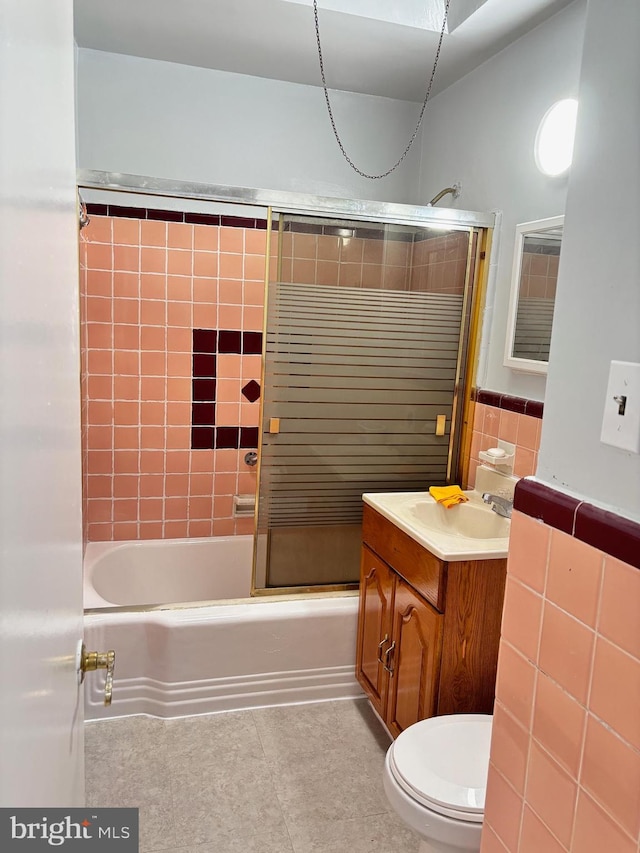 full bathroom featuring combined bath / shower with glass door, tile patterned floors, toilet, vanity, and tile walls