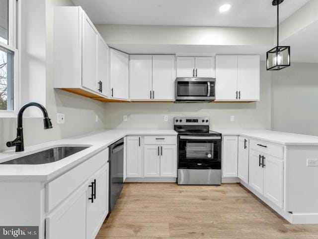 kitchen with sink, hanging light fixtures, stainless steel appliances, light hardwood / wood-style floors, and white cabinets