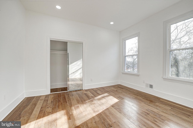 unfurnished bedroom featuring hardwood / wood-style floors, a closet, and multiple windows