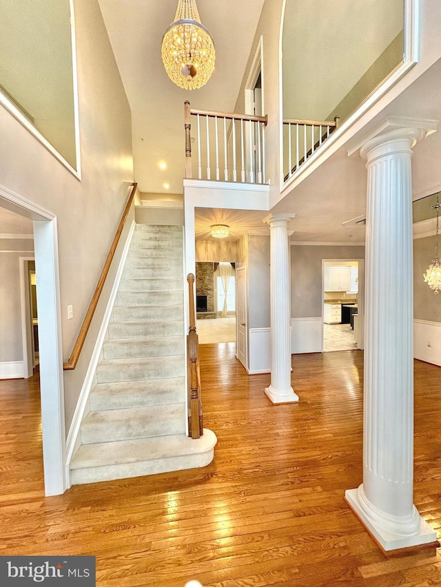 stairs featuring hardwood / wood-style floors, ornamental molding, decorative columns, and a high ceiling