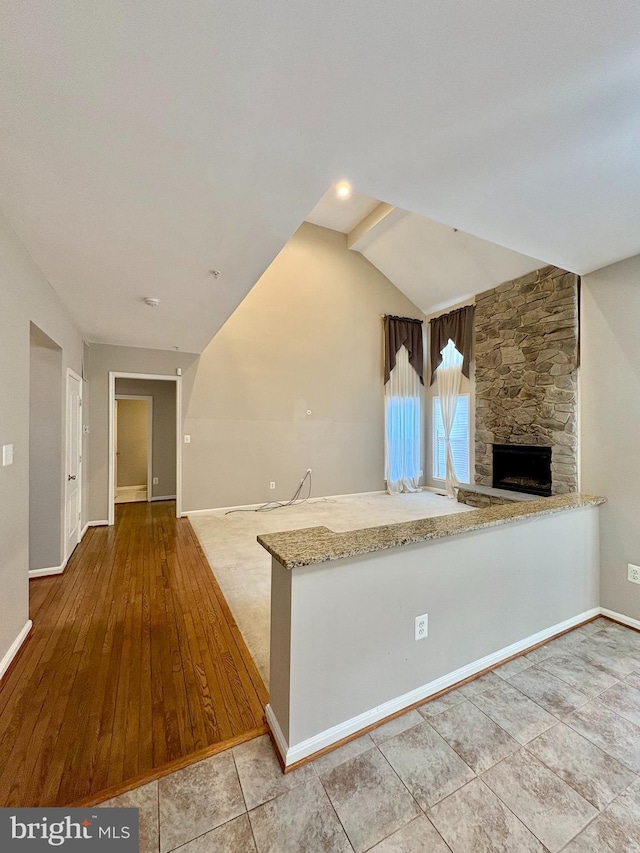 kitchen with light tile patterned floors, light stone countertops, a stone fireplace, vaulted ceiling, and kitchen peninsula