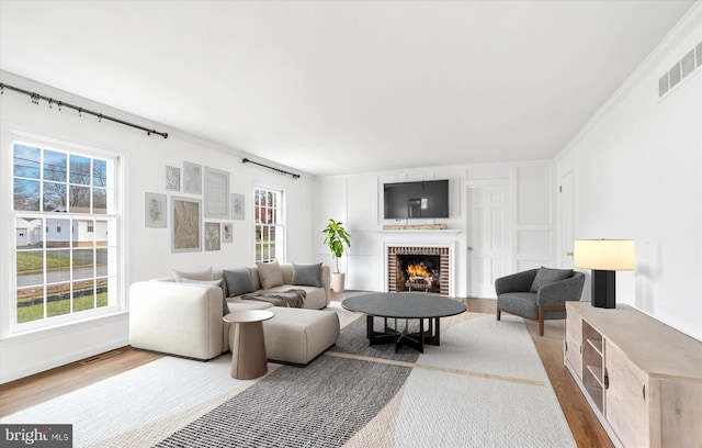 living room featuring wood-type flooring, a brick fireplace, and ornamental molding