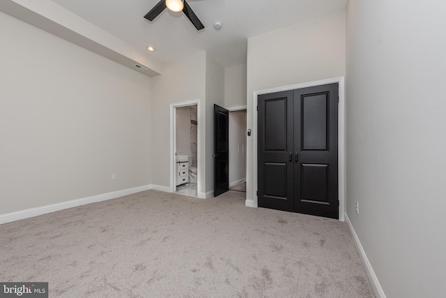 unfurnished bedroom featuring ceiling fan, light colored carpet, ensuite bathroom, and a closet