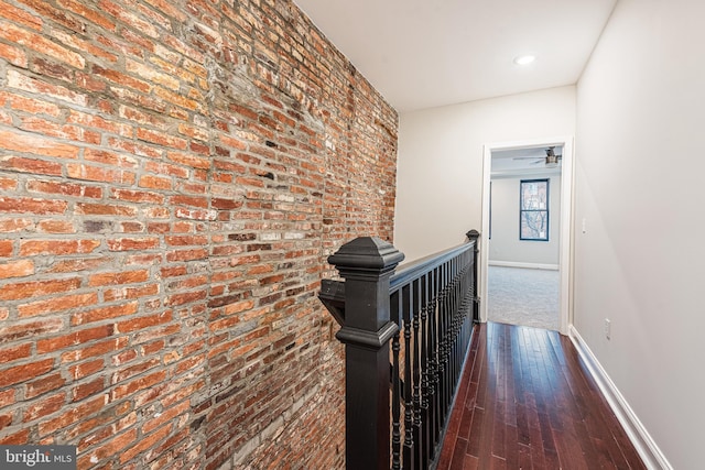 hallway with dark wood-type flooring and brick wall