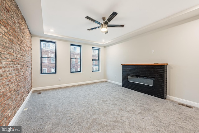 unfurnished living room featuring a raised ceiling, ceiling fan, carpet floors, and brick wall