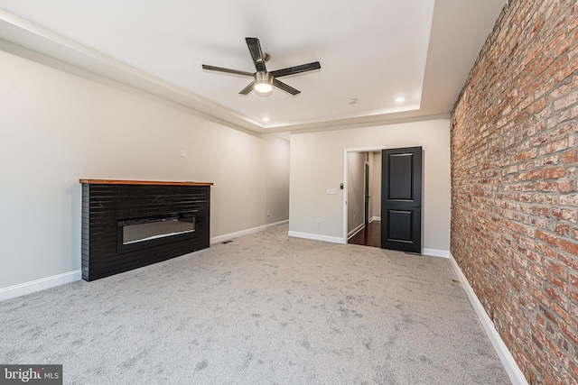 unfurnished living room featuring carpet, ceiling fan, brick wall, and a tray ceiling