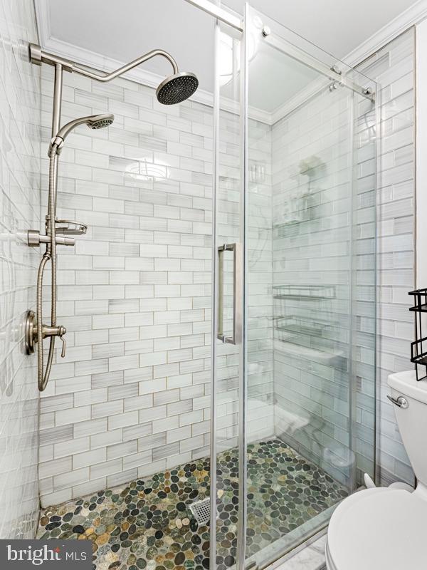 bathroom featuring toilet, a shower with door, and ornamental molding