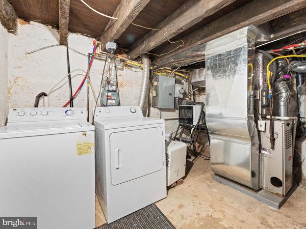 clothes washing area with electric panel, heating unit, and washer and dryer