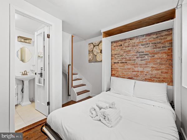 bedroom featuring light hardwood / wood-style flooring, brick wall, and sink