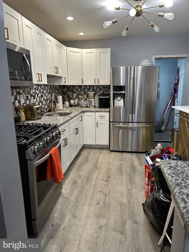 kitchen featuring white cabinetry, sink, backsplash, light hardwood / wood-style floors, and appliances with stainless steel finishes