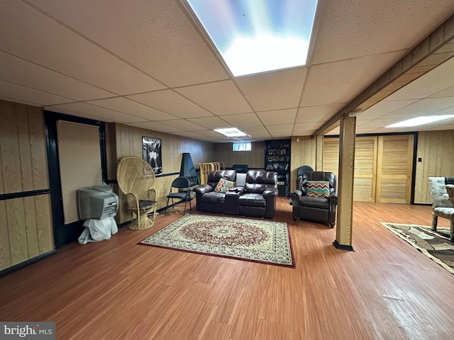 living room with hardwood / wood-style floors, a paneled ceiling, and wood walls