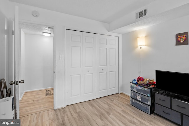 bedroom with light wood-type flooring, a textured ceiling, and a closet