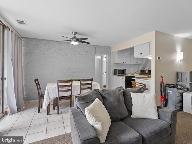 tiled living room with ceiling fan and brick wall