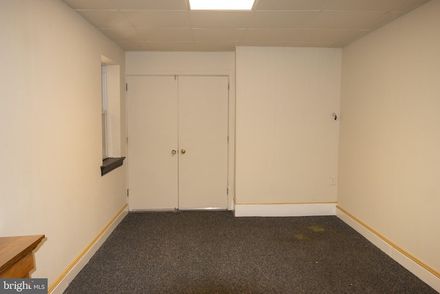 spare room with a paneled ceiling and dark colored carpet