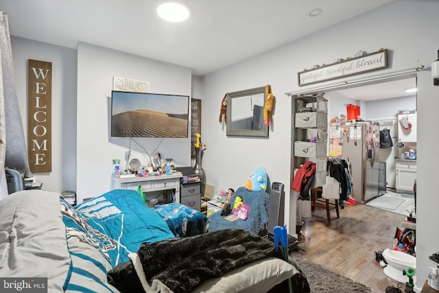 bedroom featuring stainless steel fridge and light hardwood / wood-style floors