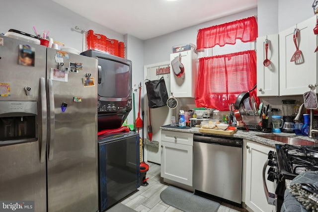 kitchen featuring white cabinets, stacked washer and dryer, decorative backsplash, light stone countertops, and stainless steel appliances