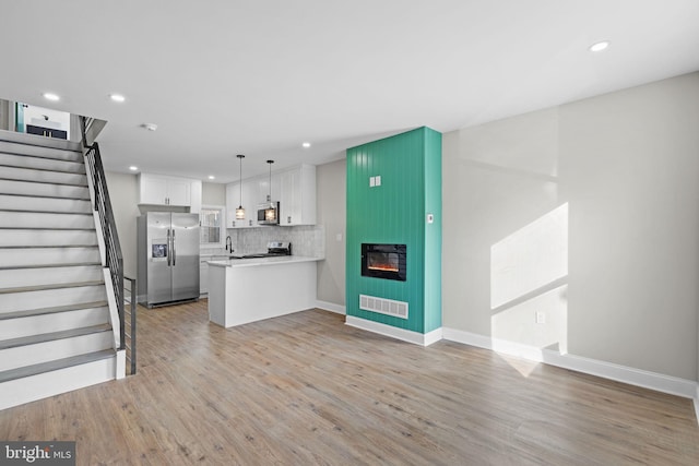 kitchen with kitchen peninsula, appliances with stainless steel finishes, light wood-type flooring, pendant lighting, and white cabinetry