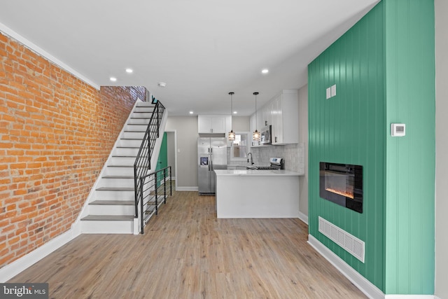 kitchen with kitchen peninsula, stainless steel appliances, pendant lighting, light hardwood / wood-style floors, and white cabinetry