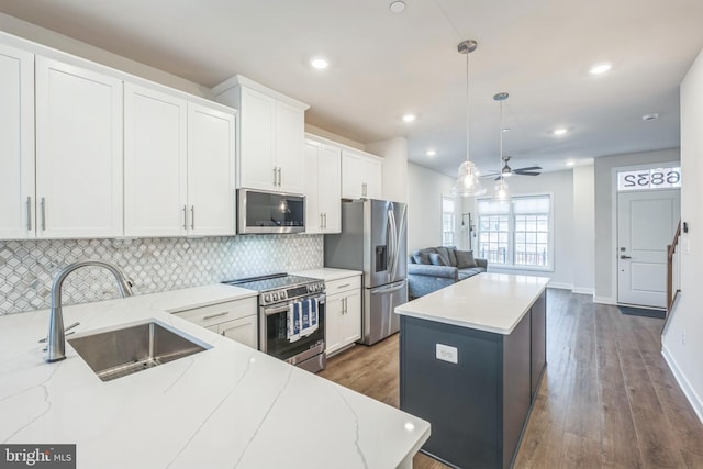 kitchen featuring hanging light fixtures, white cabinetry, light stone counters, a center island, and stainless steel appliances