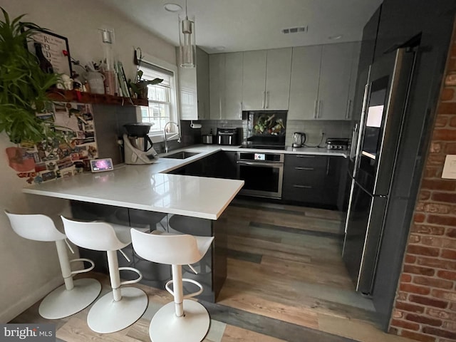 kitchen featuring gray cabinetry, sink, kitchen peninsula, oven, and hardwood / wood-style flooring