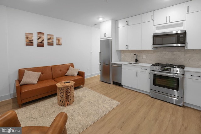 kitchen with backsplash, white cabinets, sink, appliances with stainless steel finishes, and light hardwood / wood-style floors