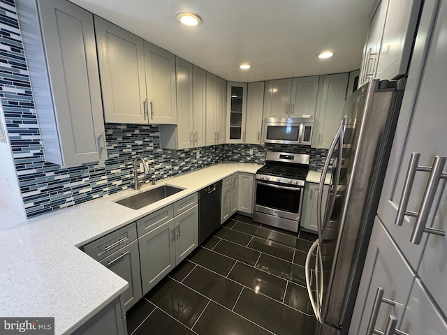 kitchen with gray cabinetry, sink, tasteful backsplash, light stone counters, and stainless steel appliances