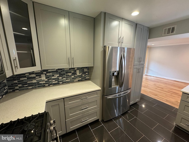 kitchen with gray cabinetry, gas range oven, dark hardwood / wood-style floors, stainless steel refrigerator with ice dispenser, and decorative backsplash