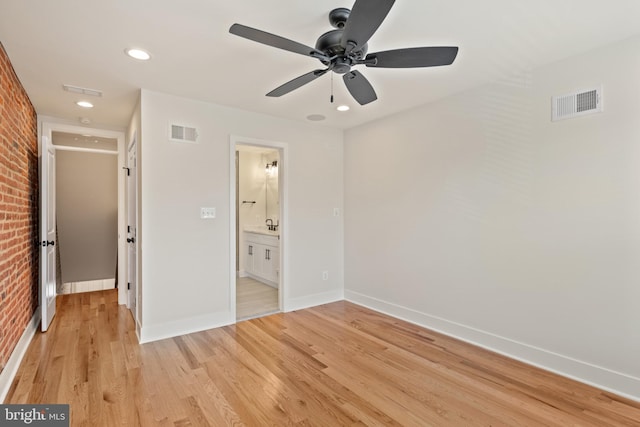 unfurnished bedroom with ceiling fan, connected bathroom, brick wall, and light wood-type flooring