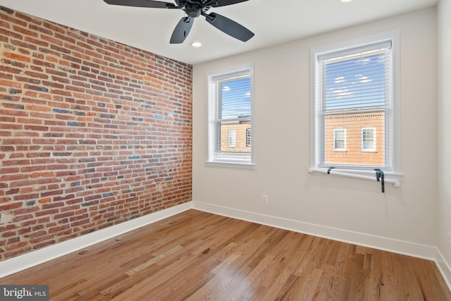 spare room with hardwood / wood-style flooring, brick wall, and ceiling fan