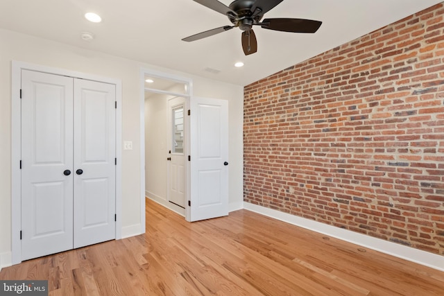 unfurnished bedroom featuring ceiling fan, a closet, brick wall, and light hardwood / wood-style flooring