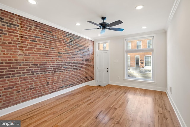 empty room with ceiling fan, light wood-type flooring, brick wall, and crown molding