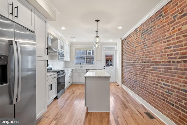 kitchen featuring white cabinetry, appliances with stainless steel finishes, decorative light fixtures, brick wall, and a kitchen island